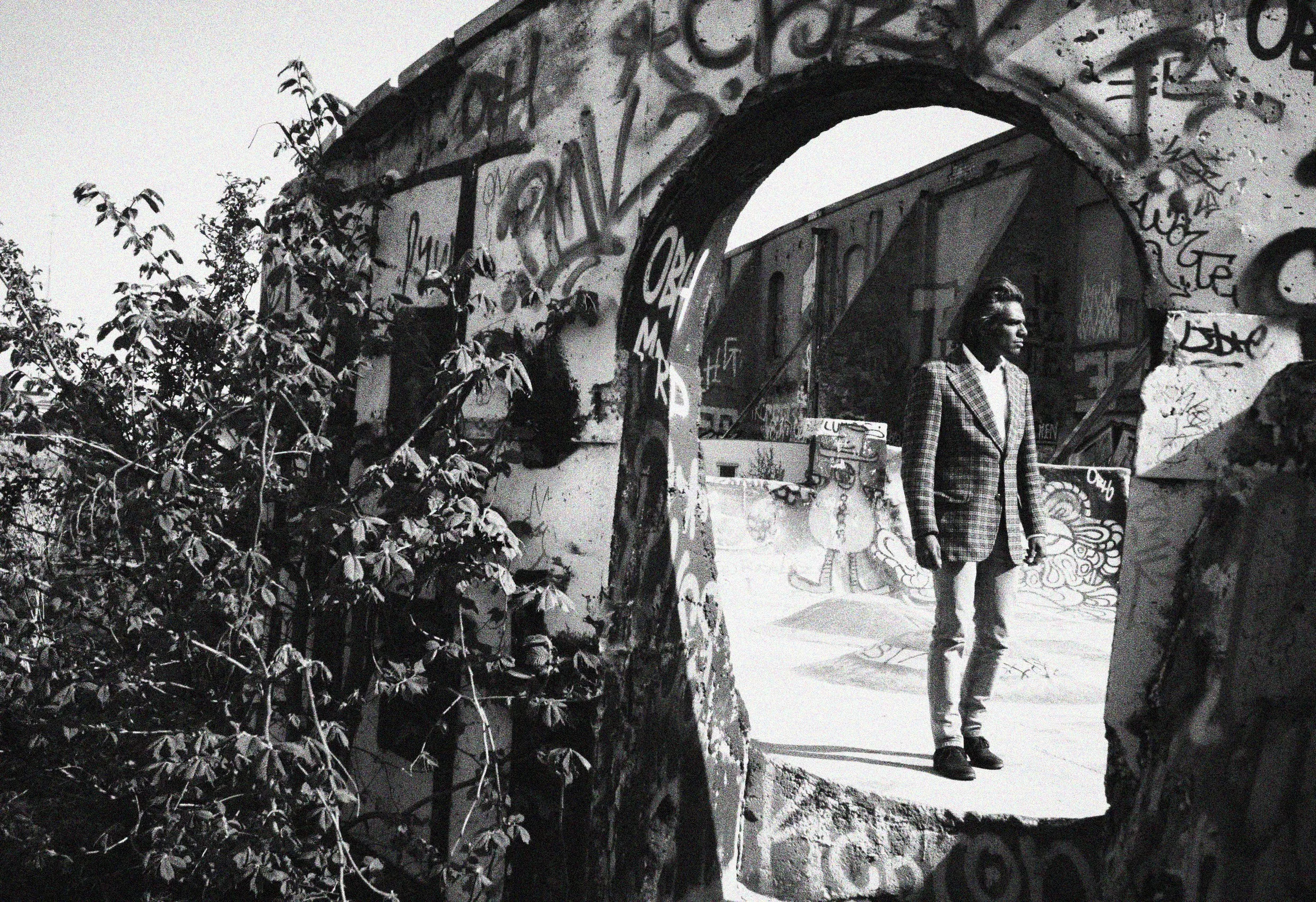 Svartvitt foto av en person i kostym i en graffitiklädd valvgång